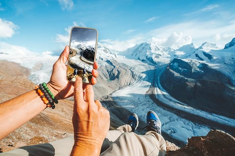 A phone held up to photograph a range of snow-covered mountains.